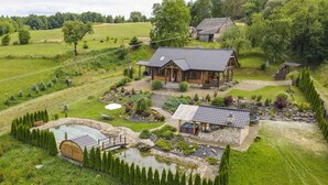 Ein großes Holzhaus mit Ziegeldach, umgeben von einem gepflegten Garten mit Teich, einer Holzterrasse und einer Steinbrücke.