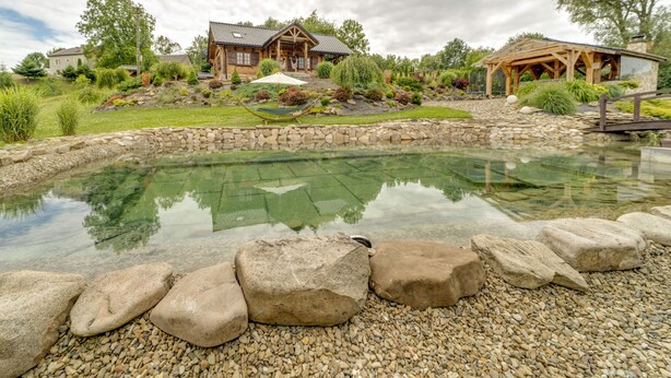 Ein Haus mit Teich, umgeben von einer Steinmauer und großen Felsen.