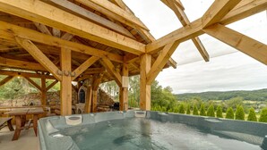 Ein Whirlpool unter einer Holzw pergola mit Steinmauern und Blick auf eine bewaldete Landschaft.