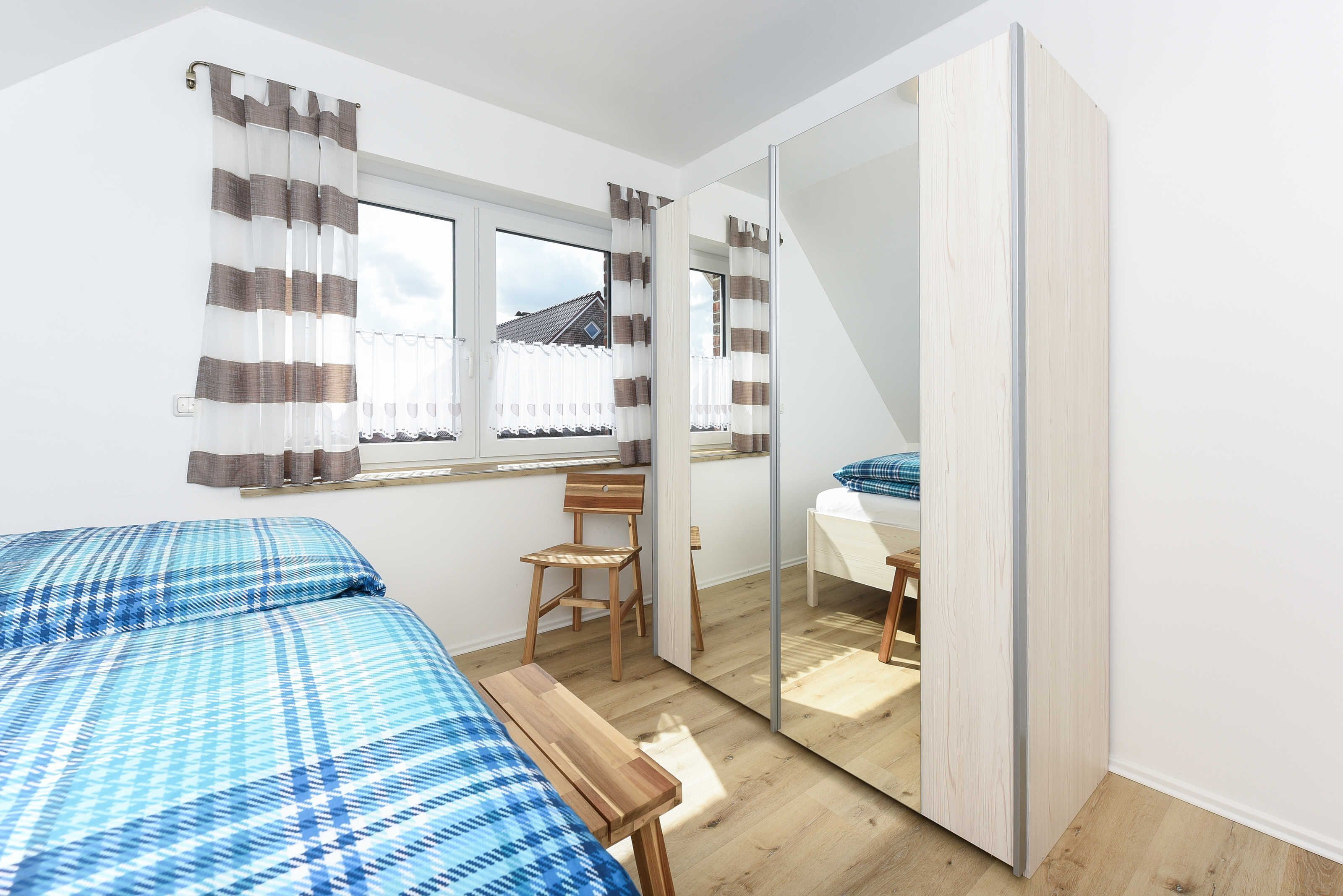Un dormitorio con dos camas, una silla de madera, una mesita, un espejo y una ventana con cortinas.