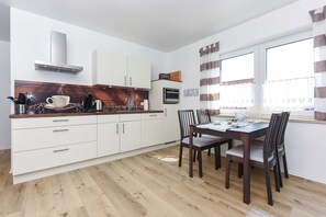 Une cuisine moderne avec des meubles blancs, un plan de travail en bois et un coin repas comprenant une table et des chaises.