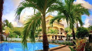 A pool surrounded by palm trees and a multi-story building with balconies.