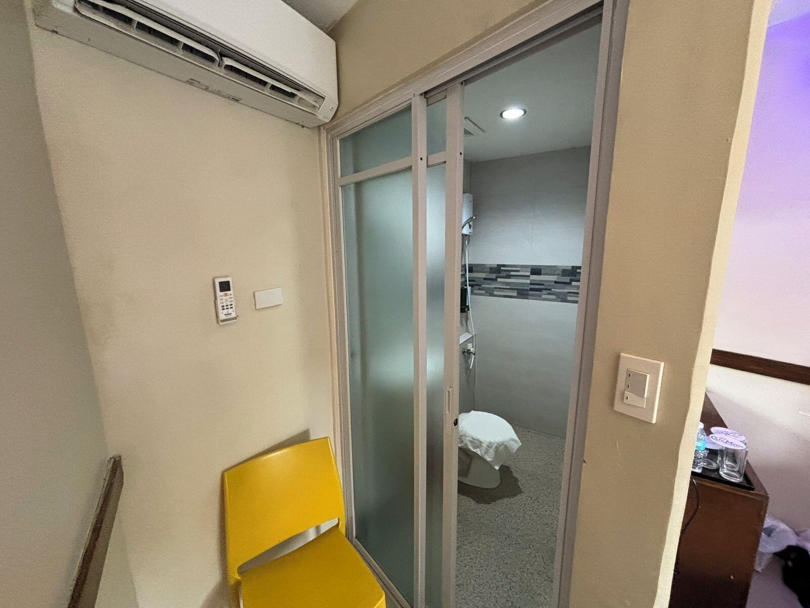 A hotel room with a sliding glass door leading to a bathroom, a yellow chair, and a small table with a bottle and glass.
