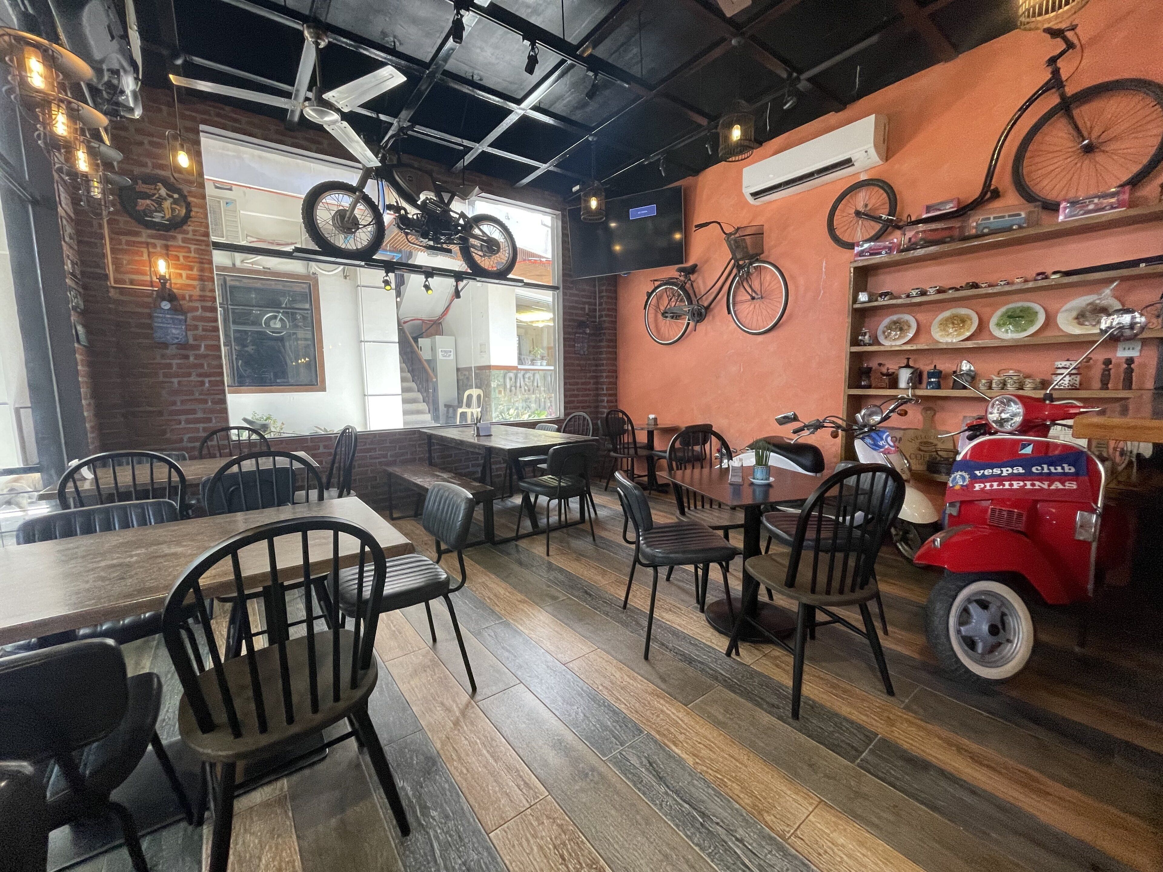 Ein Restaurantinnenraum mit Holztischen und -stühlen, einem roten Vespa-Roller und Fahrrädern, die an der Wand befestigt sind.