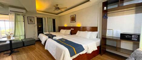 A hotel room with two beds, a desk, a sofa, and a ceiling fan.