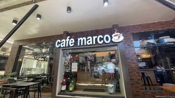 A café named 'café marco' with a glass storefront, outdoor seating, and a brick wall.