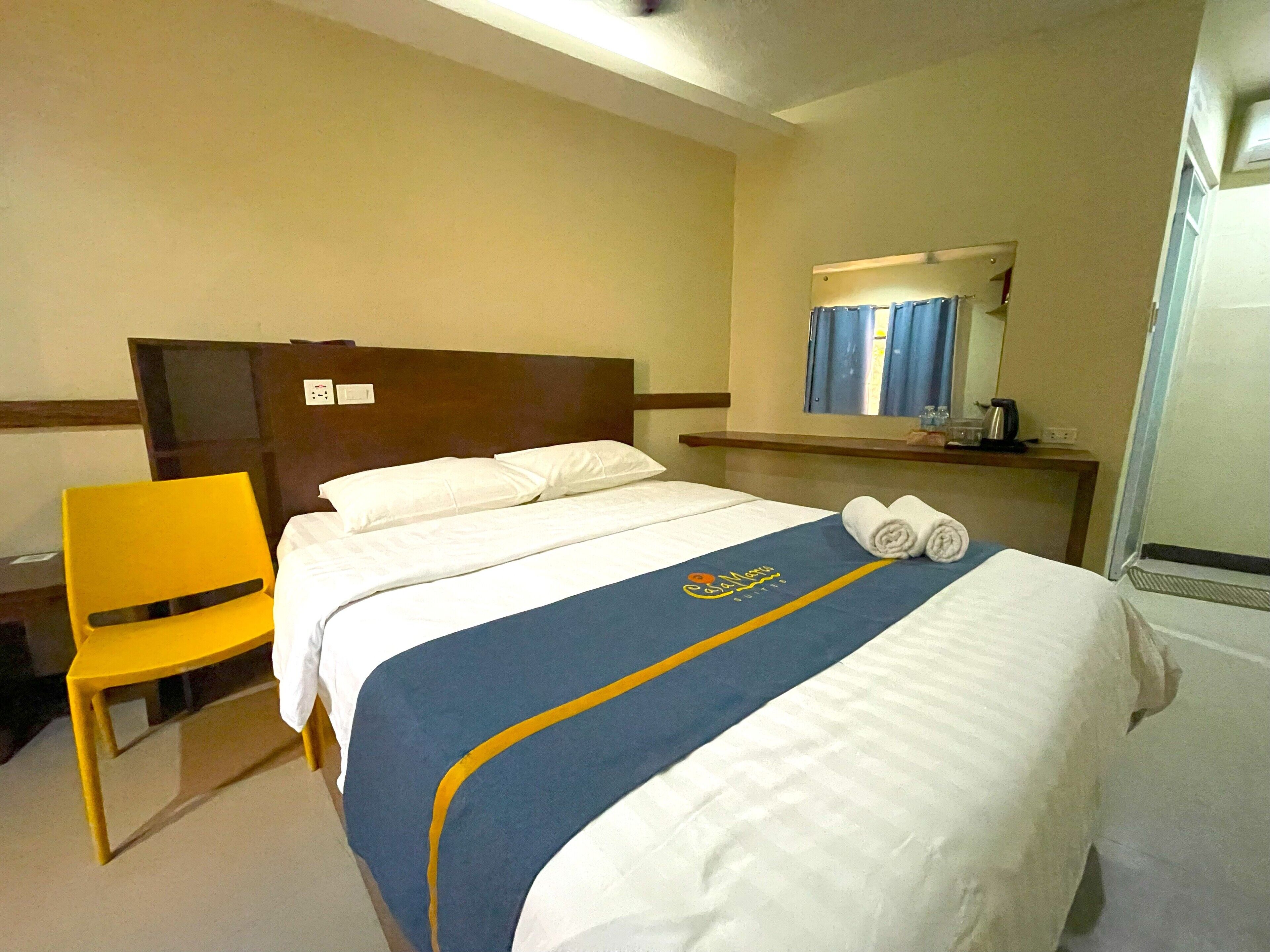 Una habitación de hotel con una cama, una silla, una mesita de noche y un espejo.