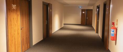 A hallway with wooden doors numbered 303 and 308, carpeted floor, and a fire extinguisher on the wall.