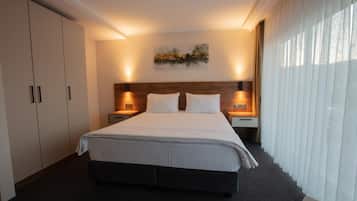 Quarto de hotel com uma cama grande, duas mesas de cabeceira, um criado-mudo e uma cabeceira de madeira, com um quadro na parede.
