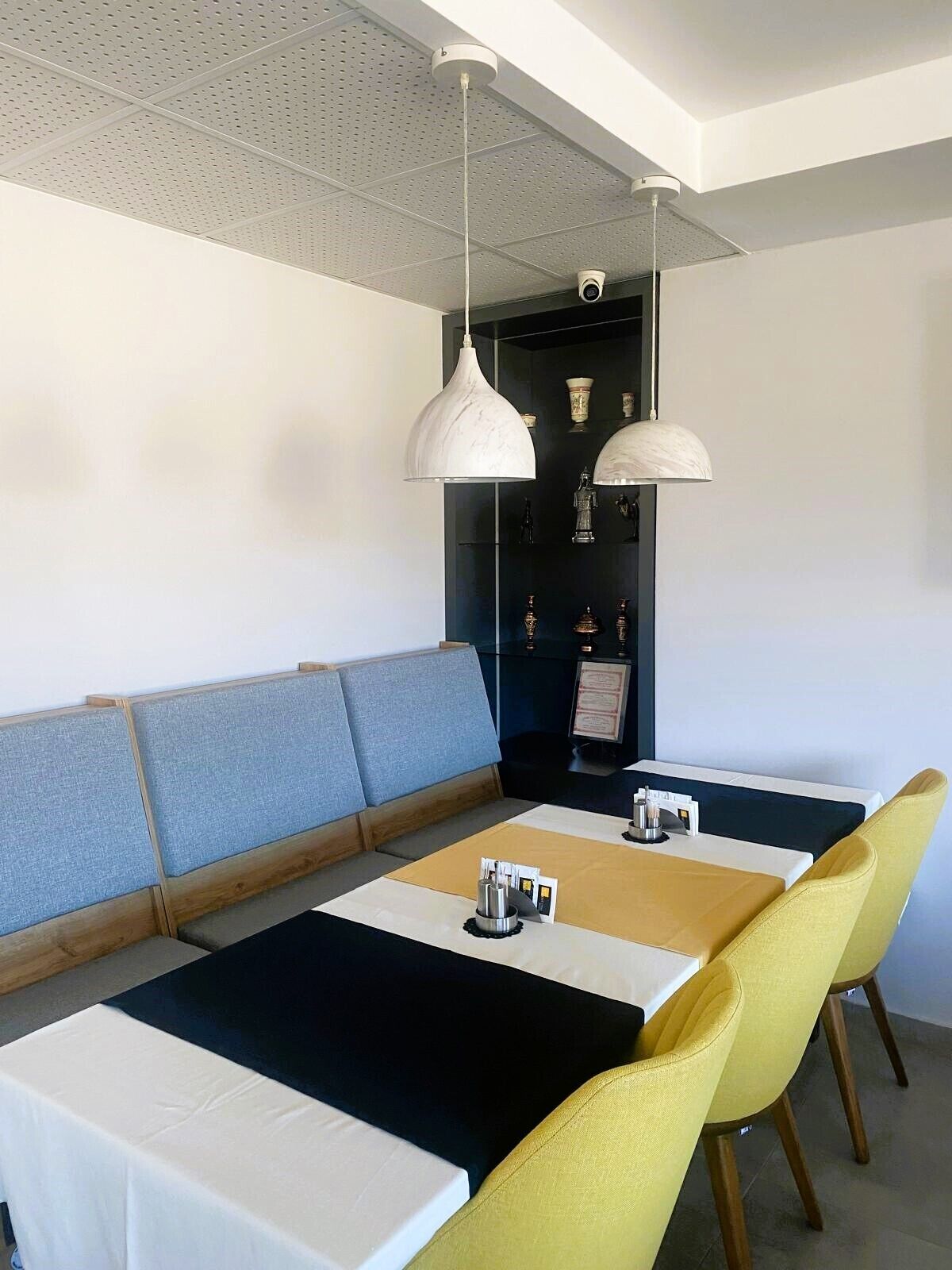 A modern dining area with a long table, yellow chairs, and a blue cushioned bench.