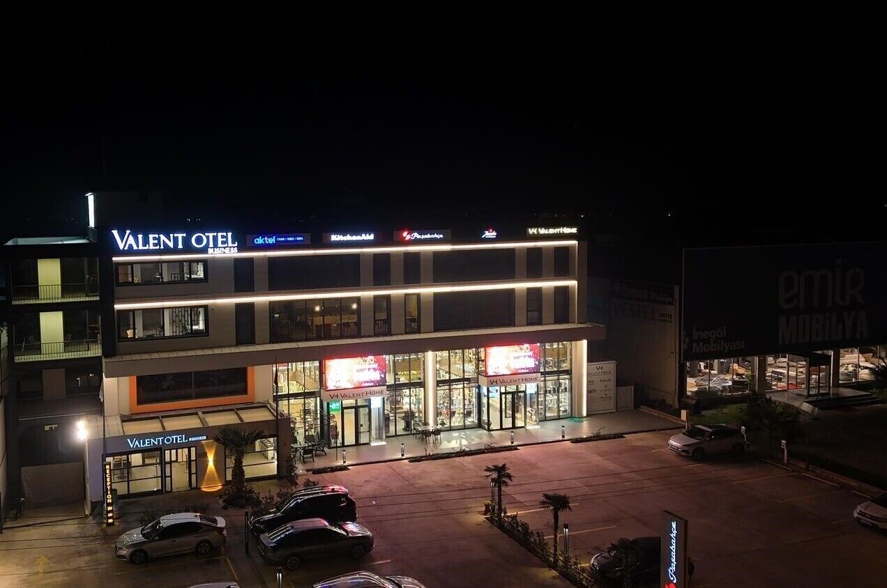 A multi-story hotel named "Valentotel" with a modern design, featuring a prominent sign and multiple ground-level shops.