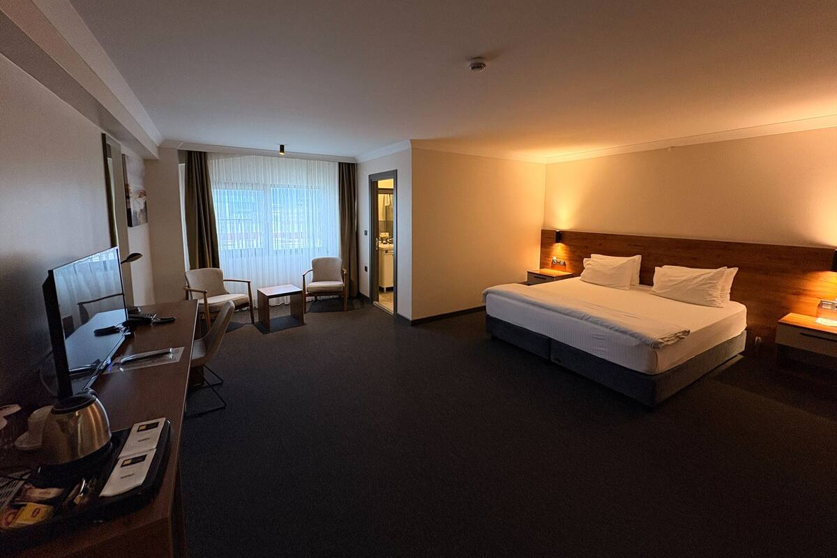 A hotel room with a bed, a desk with a computer, a chair, and a window with curtains.