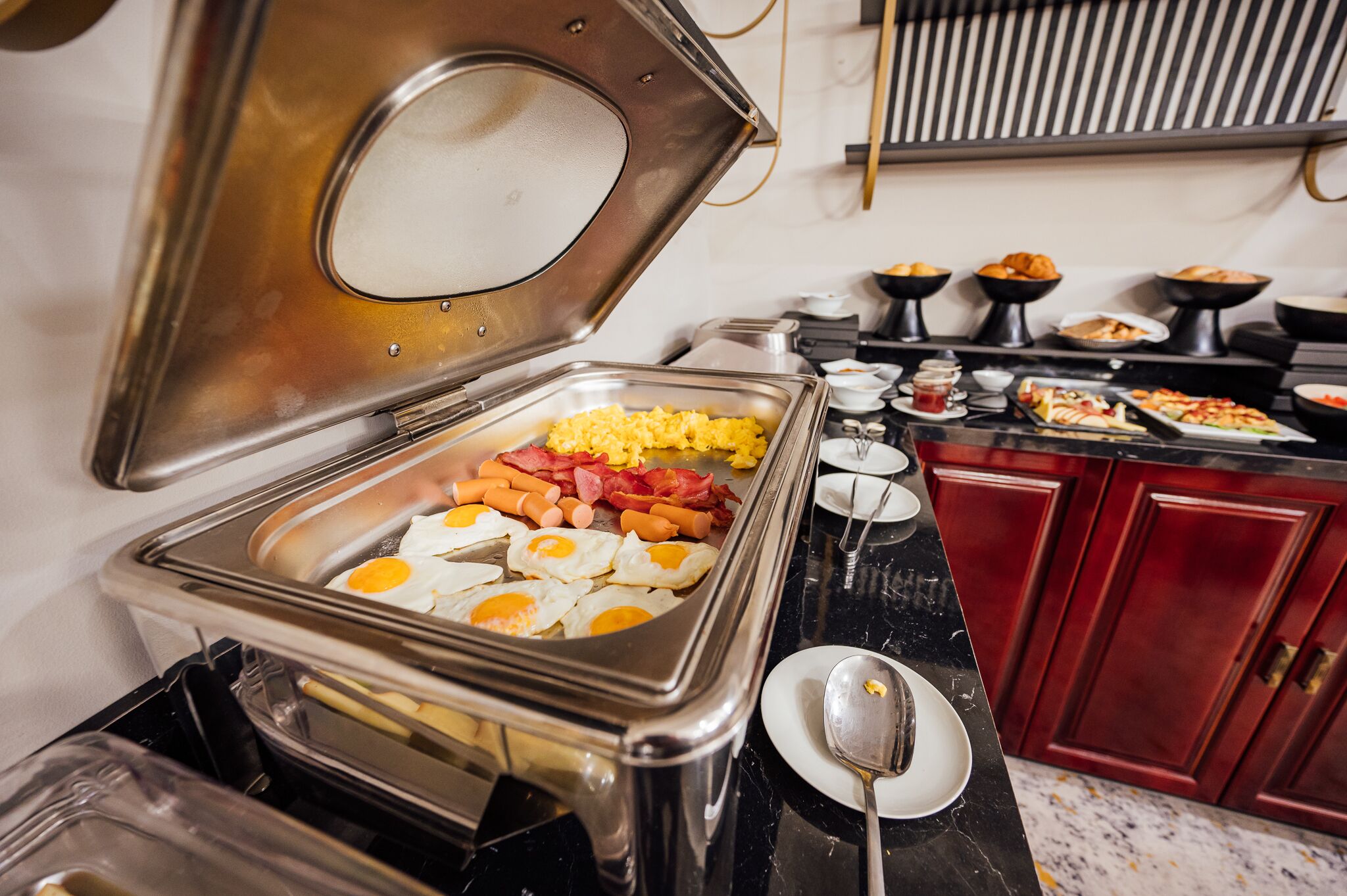 A buffet setup with various food items including eggs, sausages, and vegetables.