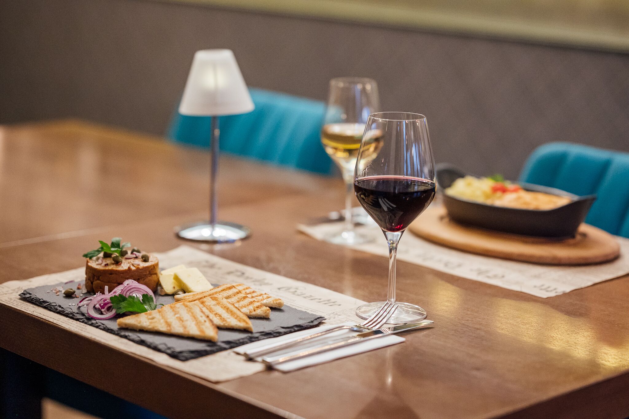 Ein Esstisch mit verschiedenen Speisen, darunter ein Sandwich, eine Salatschüssel und ein Glas Rotwein.