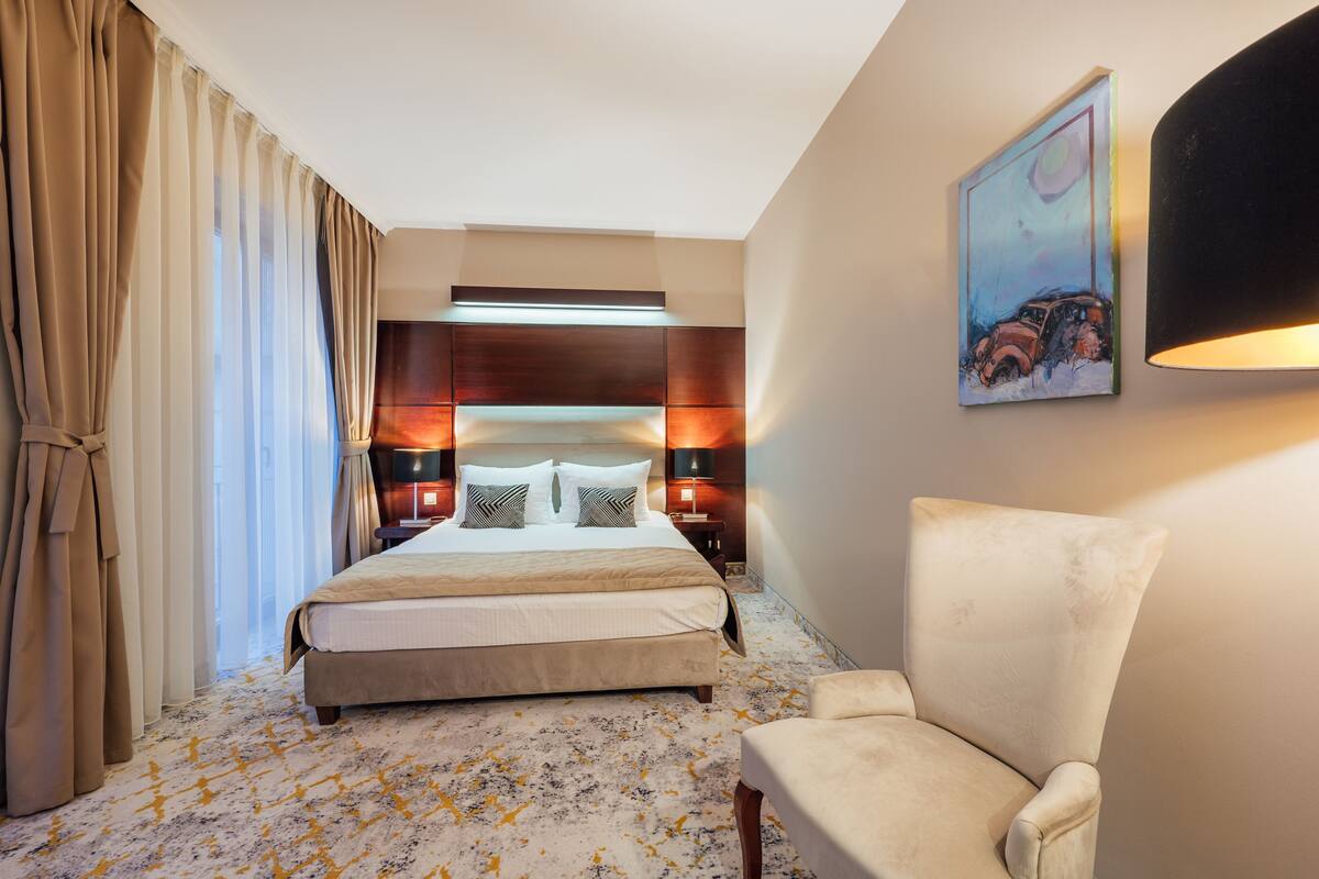 A hotel room with a large bed, a chair, a painting on the wall, and a ceiling light.