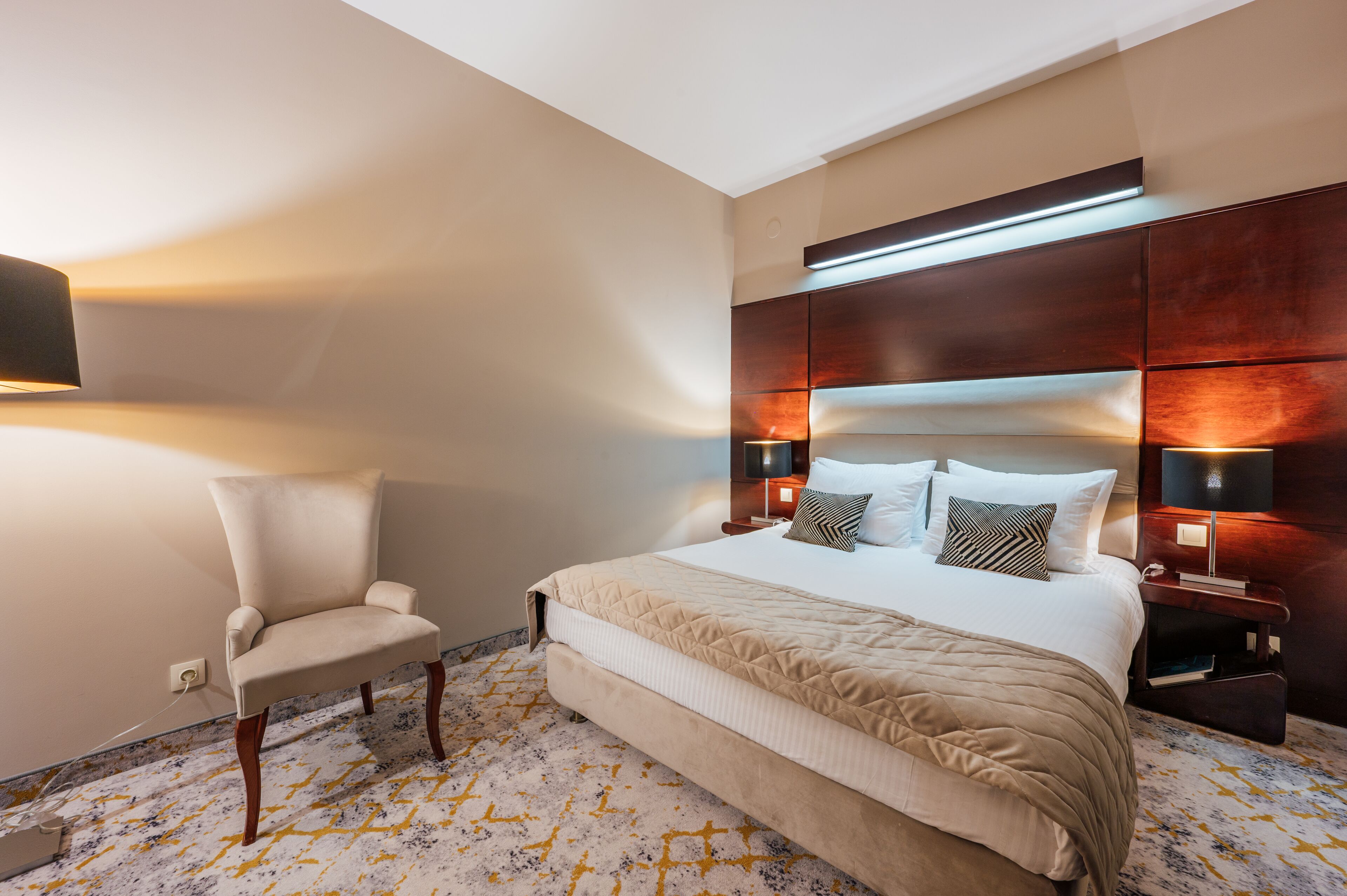 A hotel room with a large bed, a chair, and a nightstand with a lamp.