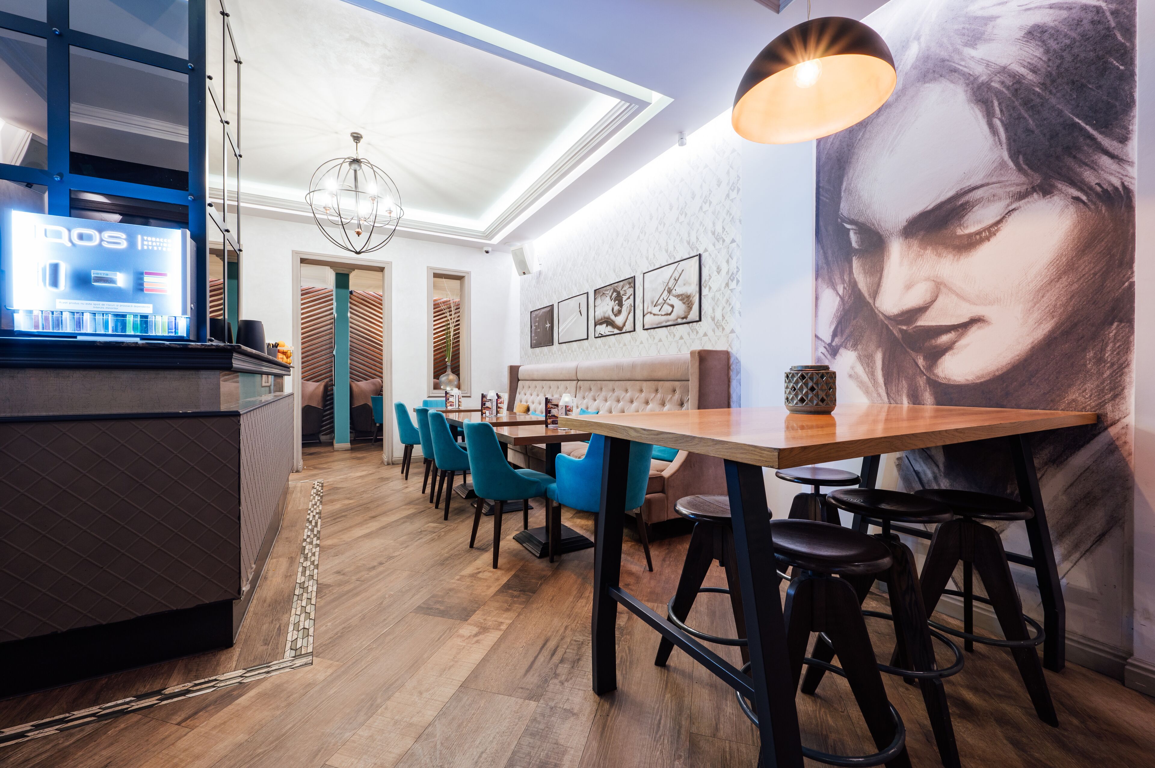 Interior moderno de restaurante com área de bar, piso de madeira, cadeiras azuis e um grande mural na parede.