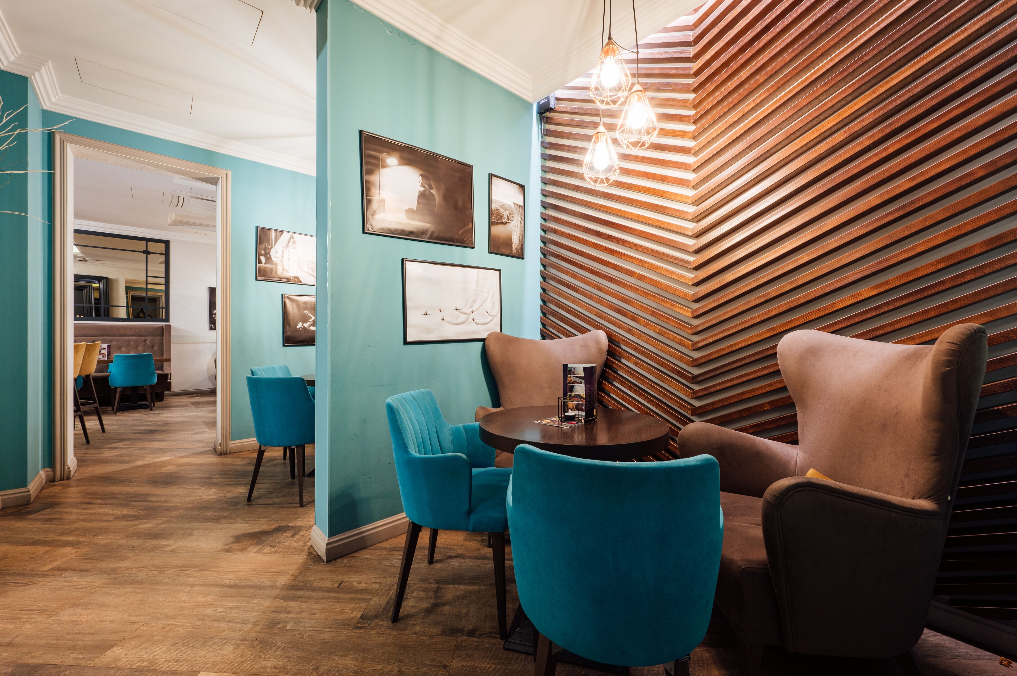 A modern interior with teal walls, a wooden slatted wall, and blue and brown chairs around a small table.