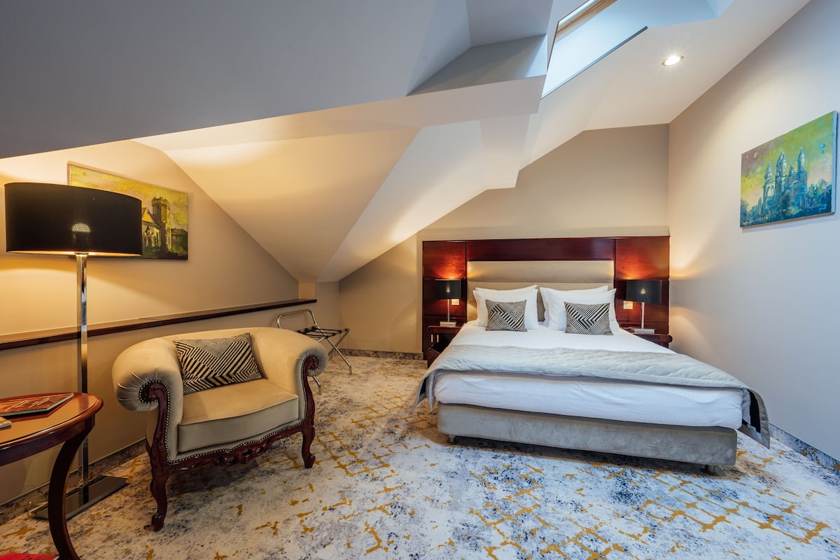 A bedroom with a bed, a chair, a lamp, and a painting on the wall.