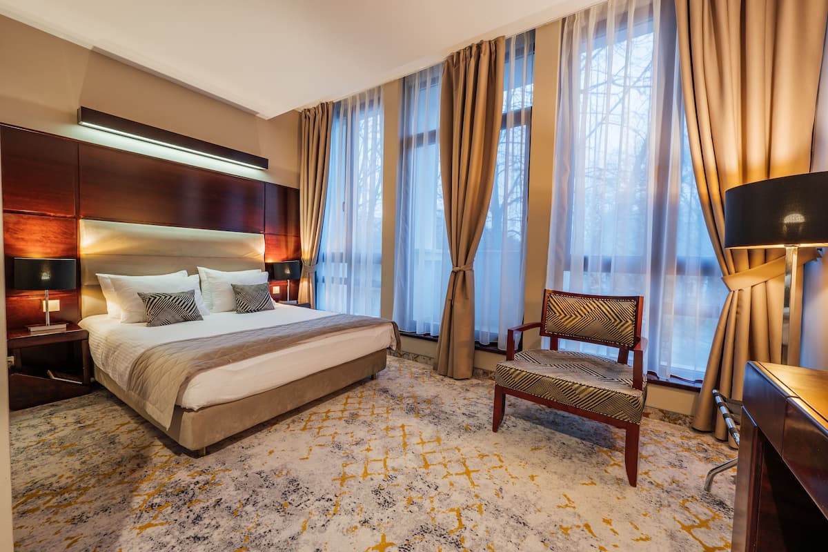 A hotel room with a large bed, a chair, a desk, and a window with curtains.