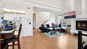 A spacious living area with a fireplace, a dining table with chairs, and a kitchen in the background.