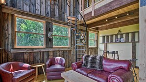Un interior rústico de madera con un sofá y dos sillones de cuero, una mesa de madera y una escalera en espiral.