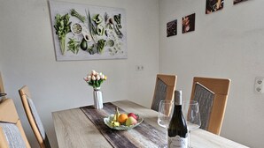A dining table with a wooden table runner, a bottle of wine, and a fruit bowl. - Vacation apartment Alpenvorland am Lech  (Apfeldorf)