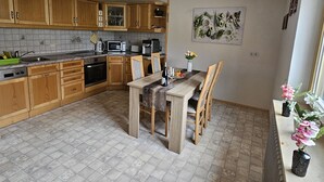 A kitchen with wooden cabinets, a dining table with chairs, a microwave, and a coffee machine. - Vacation apartment Alpenvorland am Lech  (Apfeldorf)