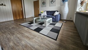 A modern living room with a glass coffee table, a blue sofa, and a patterned rug. - Vacation apartment Alpenvorland am Lech  (Apfeldorf)