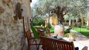 A courtyard with stone walls, wooden furniture, a large tree, and a barrel. - Exclusive Pool Villa - Cascina Relais (Sicilia)