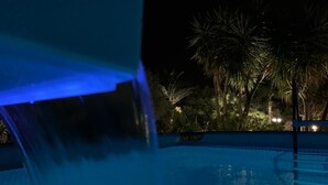 A nighttime pool area with a water feature and palm trees in the background. - Exclusive Pool Villa - Cascina Relais (Sicilia)
