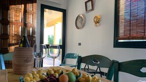 A dining table with a fruit platter, wine glasses, and a bottle. There are chairs around the table, and a window with blinds. - Exclusive Pool Villa - Cascina Relais (Sicilia)