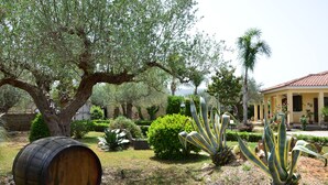 A garden with a large tree, a barrel, and a building with a tiled roof. - Exclusive Pool Villa - Cascina Relais (Sicilia)