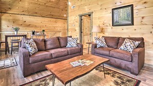 Ein gemütliches Blockhaus-Interieur mit zwei braunen Sofas, einem Holztisch und einem gerahmten Bild eines Waldes an der Wand.