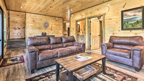 Ein Holzblockhaus-Interieur mit zwei Ledersofas, einem Holztisch und einem Deckenventilator.