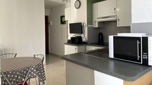 Une cuisine compacte équipée d’un four à micro-ondes, d’une machine à café et d’un téléviseur. Un coin repas avec une table et des chaises est également à disposition.