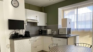 Une cuisine compacte avec des meubles blancs, un four à micro-ondes, un grille-pain et une machine à café. On y trouve une table à manger avec une nappe à pois et des chaises en métal.