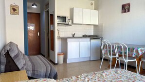 A compact living space with a kitchenette, a dining area with a table and chairs, and a bed with a floral bedspread. - Cozy Studio Near Thermal Baths with Balcony, A/C, and Modern Amenities (Balaruc-les-Bains)
