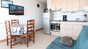 A compact kitchen with a dining area, a sofa, and a TV displaying a news program. - Studio in Balaruc-les-Bains with AC and Wifi (Balaruc-les-Bains)