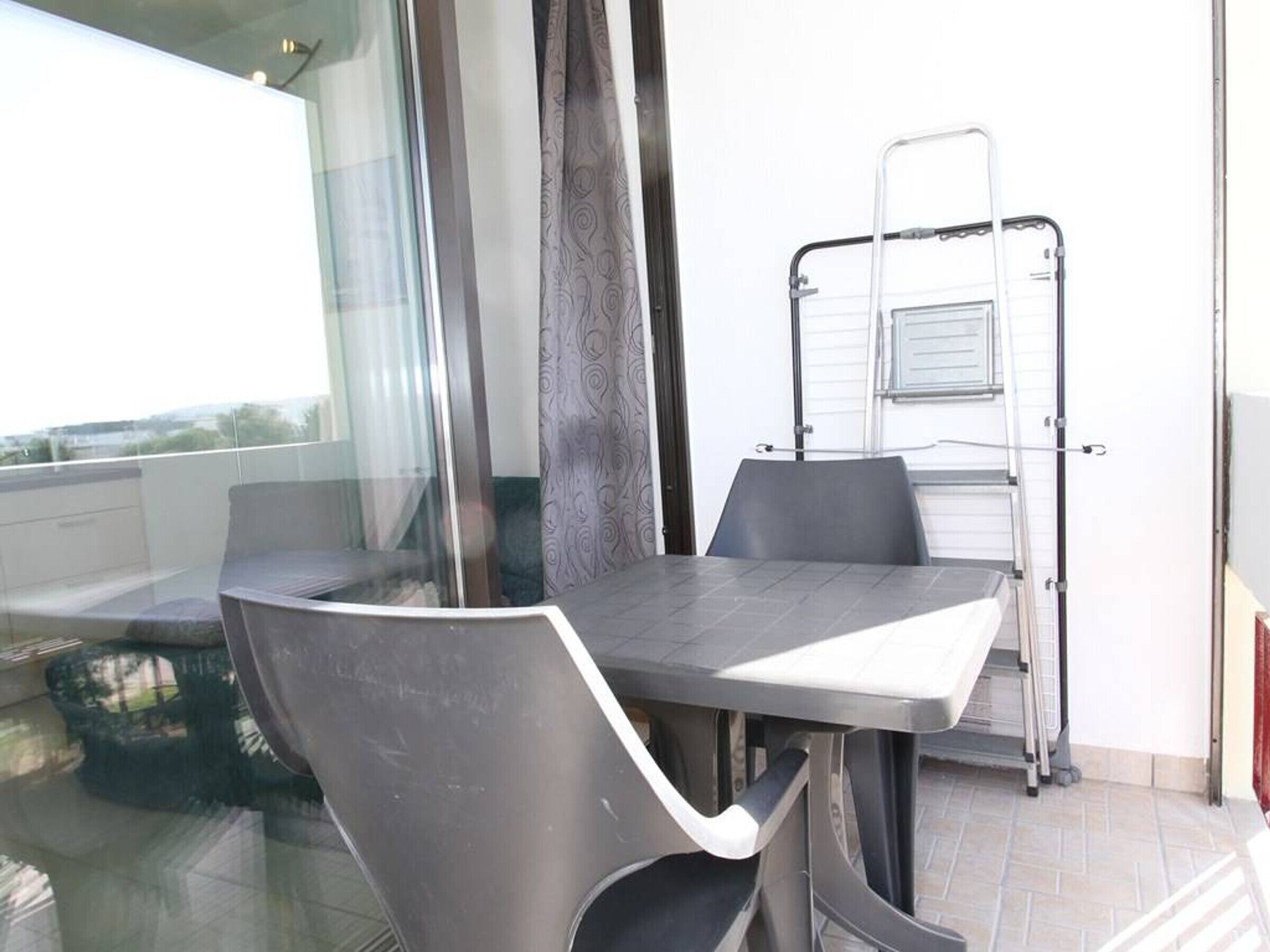 A balcony with a table and chairs, a glass door, and a metal ladder.