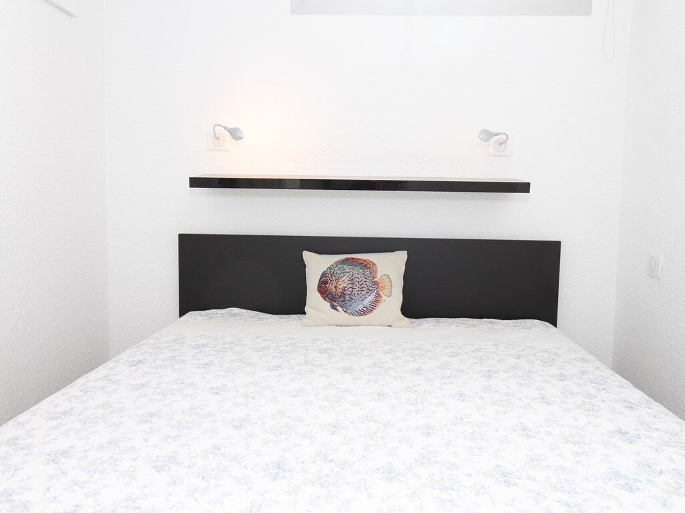 A bedroom with a bed, a pillow with a fish design, and two bedside lamps.