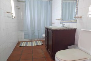 A small bathroom with white tiled walls, a dark wooden cabinet, a white sink, a toilet, and a shower curtain.