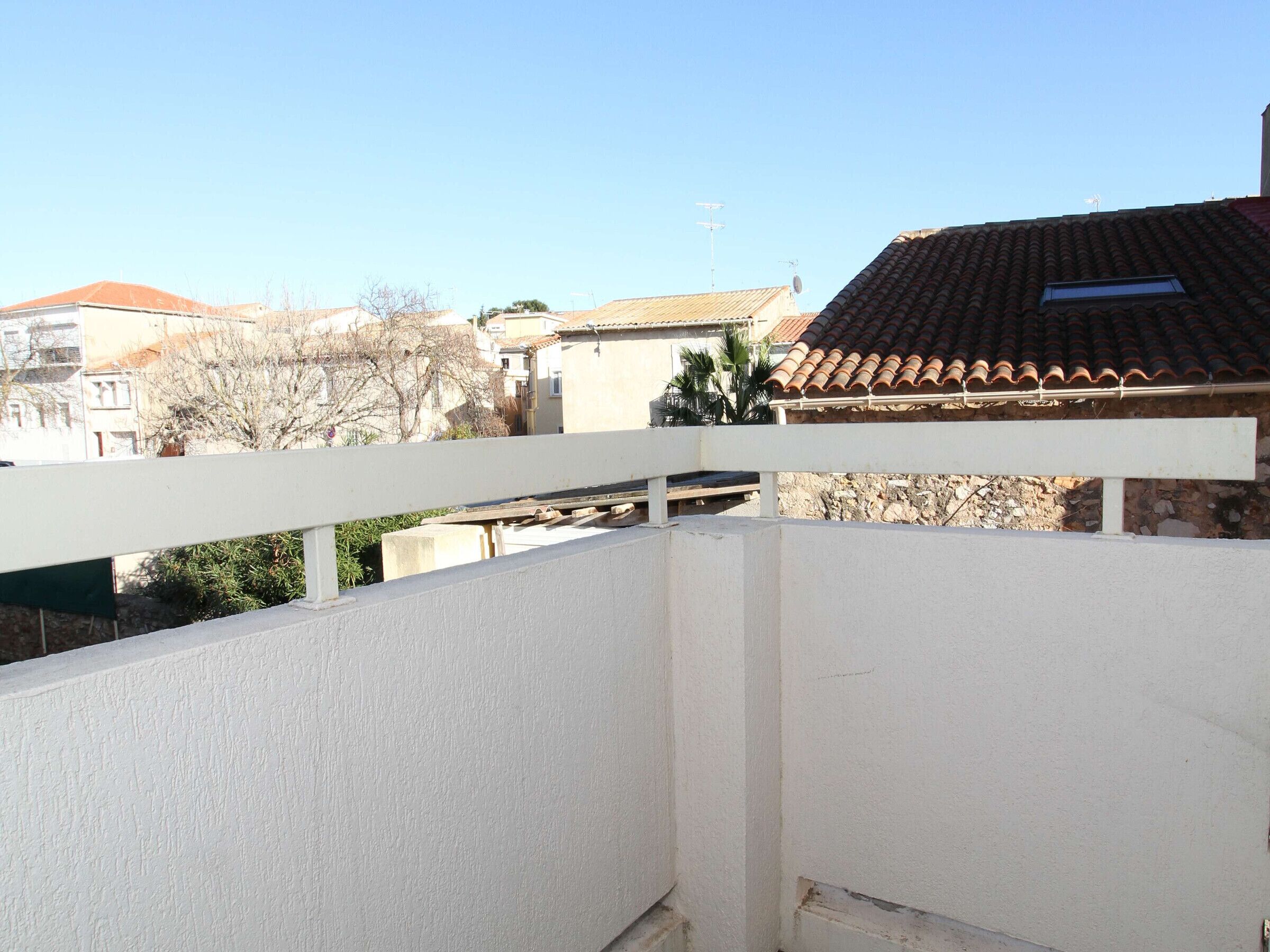 Een balkon met een witte reling, met uitzicht op een woongebied met huizen en een heldere lucht.