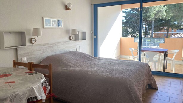 Ein Schlafzimmer mit einem Bett, einem Tisch mit Tischdecke, einem Stuhl, einer Wandlampe und einem Bilderrahmen.