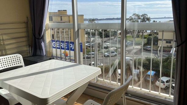 A balcony with a table and chairs, a view of a parking lot, and a building with a sign that reads "GEREPA". - Lovely 1-bedroom apartment with open view, loggia, elevator and wifi in Balaruc-les-Bains (Balaruc-les-Bains)