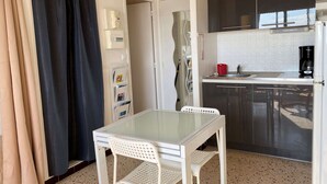 A compact kitchen with a modern design, featuring a white table and chair, a coffee maker, and a refrigerator. - Lovely 1-bedroom apartment with open view, loggia, elevator and wifi in Balaruc-les-Bains (Balaruc-les-Bains)