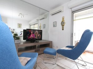 A modern living room with a flat-screen TV, blue chairs, a wooden entertainment unit, and a large mirror. - Charming T1 Apartment with A/C, 100m from Thermal Baths, Fully Equipped Kitchen, Private Loggia (Balaruc-les-Bains)