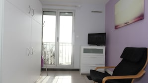 A room with a sliding glass door leading to a balcony, a white cabinet with drawers, a black chair, and a television on a stand. - Air-conditioned studio with WIFI in Balaruc-les-Bains (Balaruc-les-Bains)
