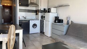 En kompakt bolig med tekøkken, vaskemaskine, køleskab, sofa og spisebord.