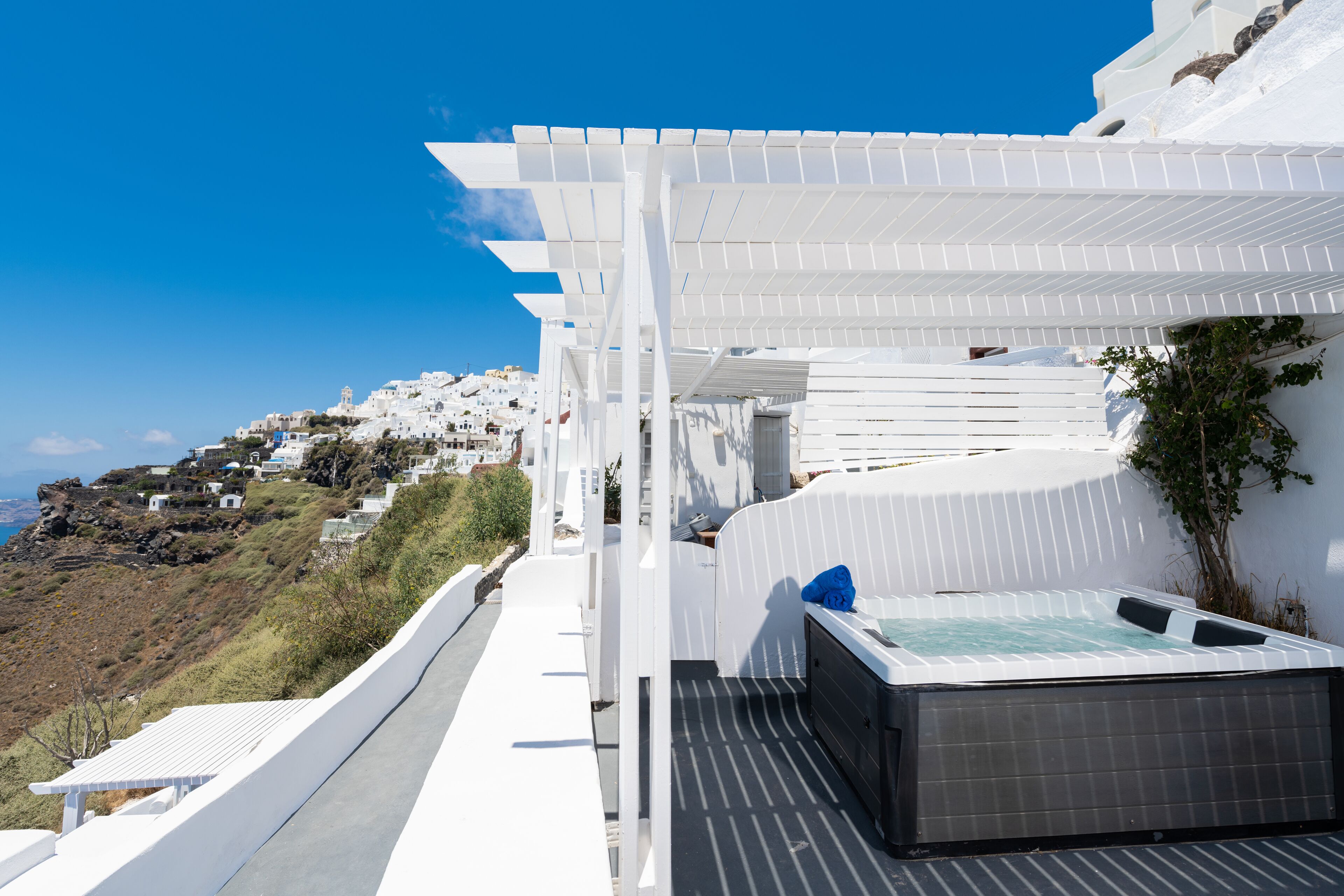 Una terraza en la azotea con jacuzzi, paredes blancas y vistas a un pueblo blanco en una colina.